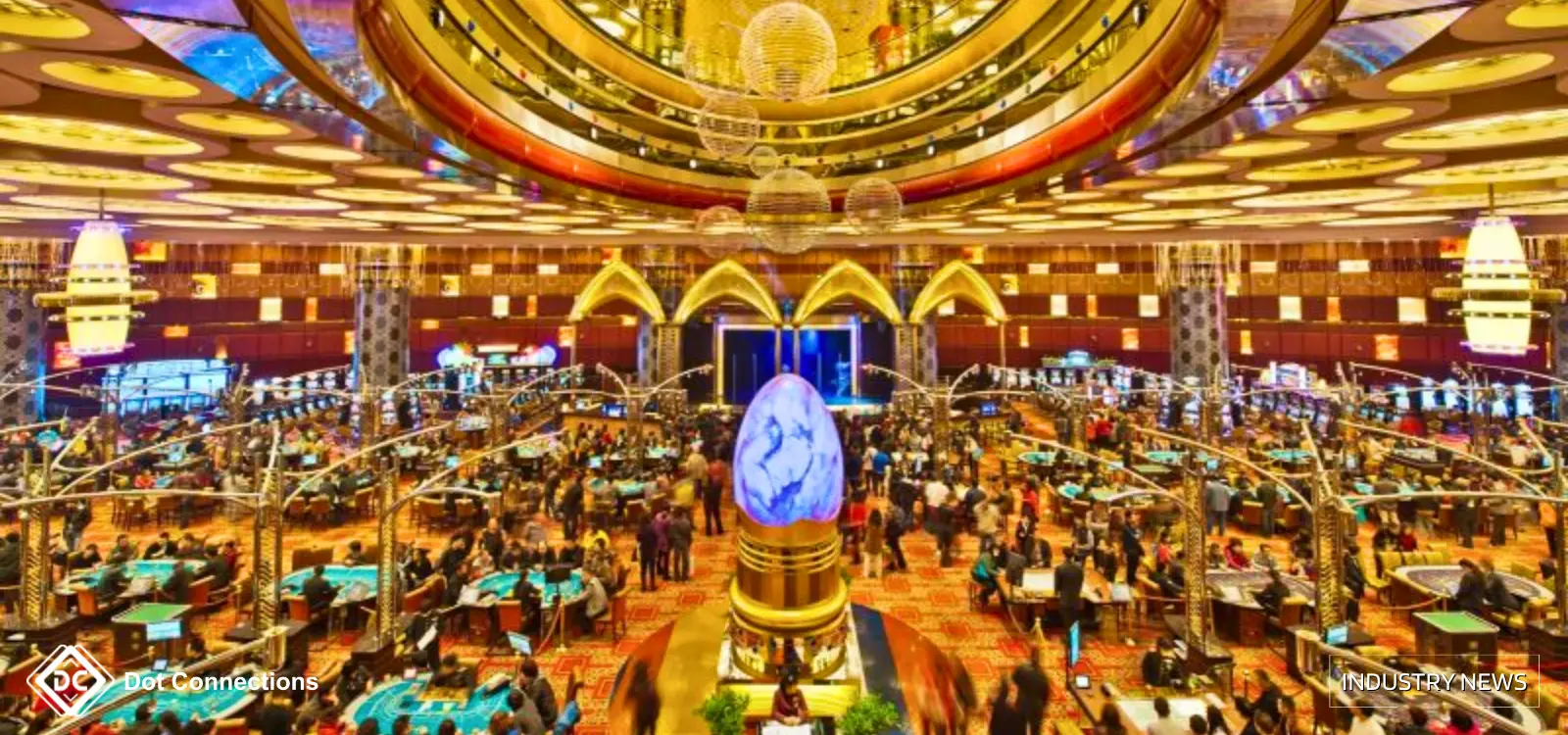Bustling casino interior with many baccarat tables, players and central decorative sculpture.