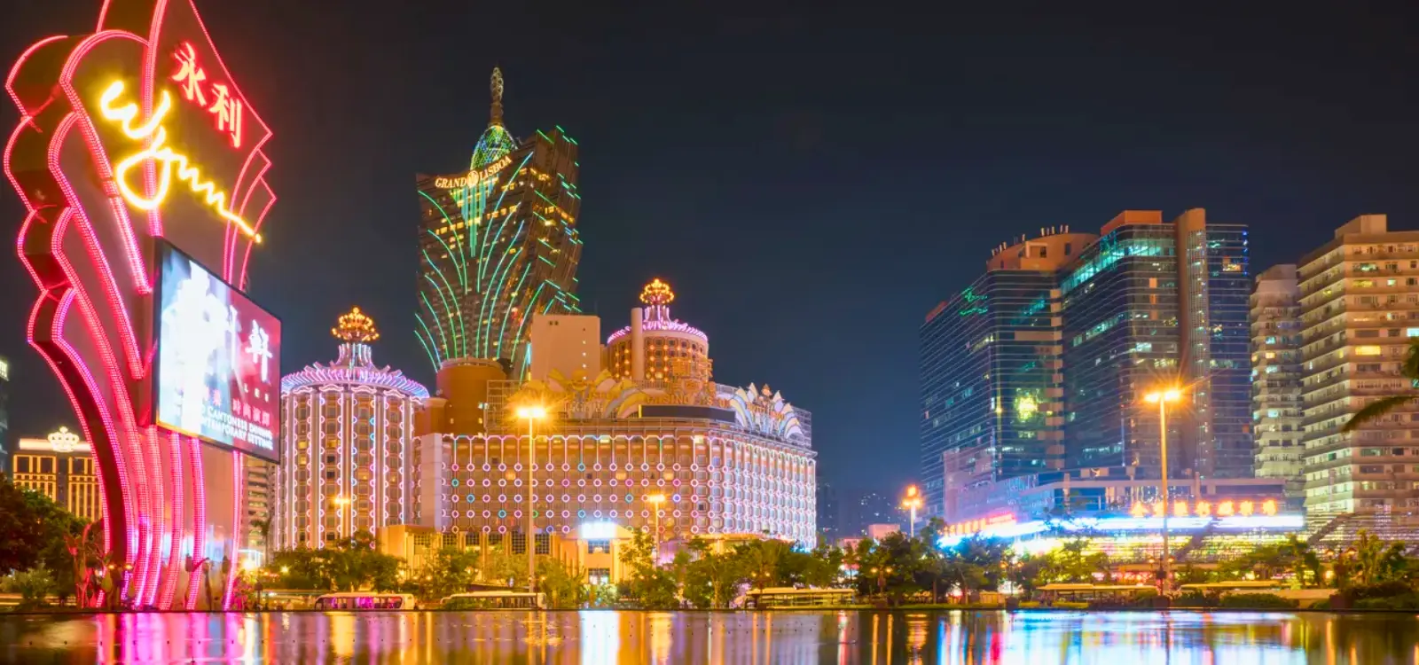 Night view of Macau’s casino district with illuminated hotel towers, neon lights, and waterfront reflections.